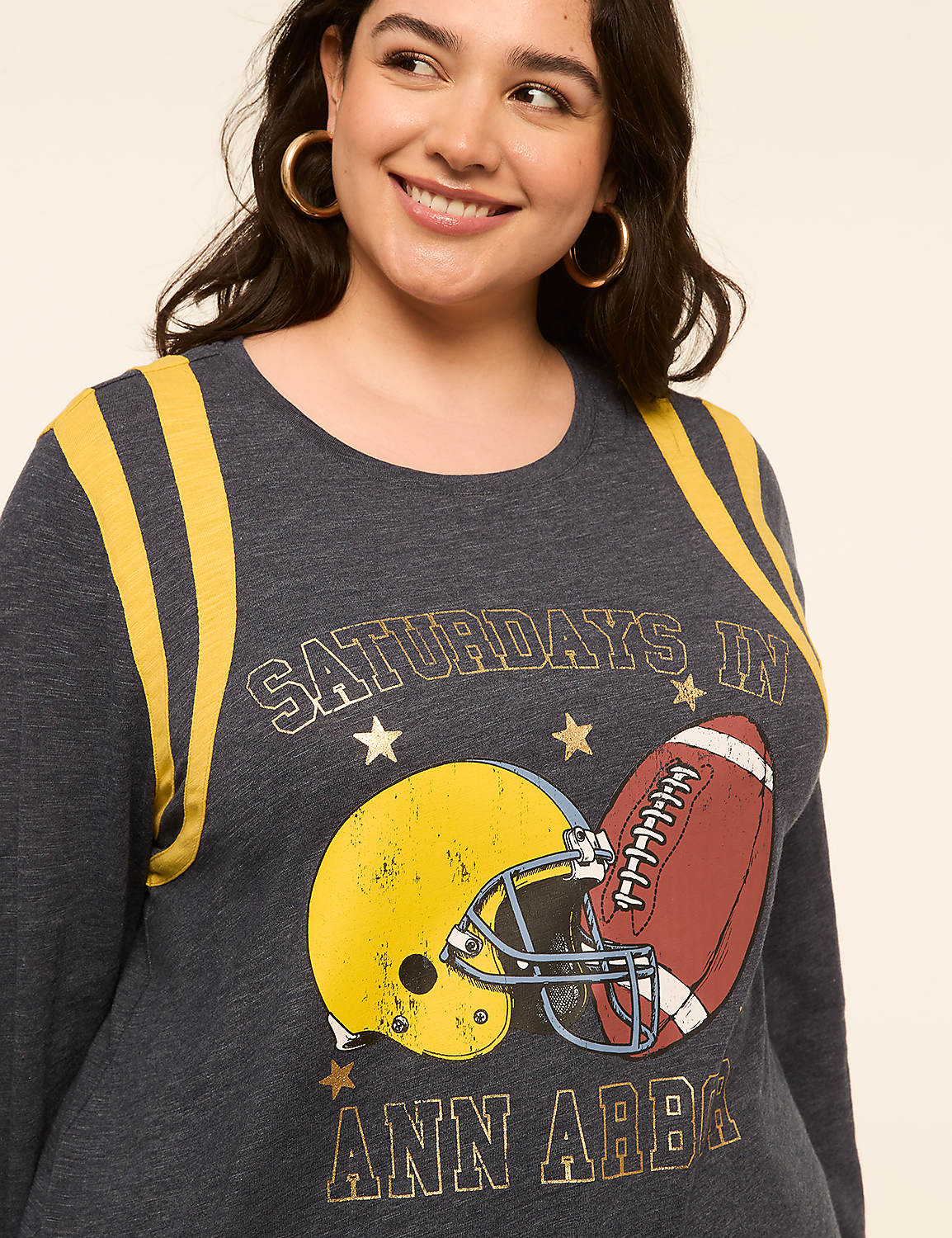 A woman smiles in the foreground, wearing a dark blue sweatshirt with a graphic of a football helmet and ball, while the background is a plain, light-colored studio backdrop. Product Image 4