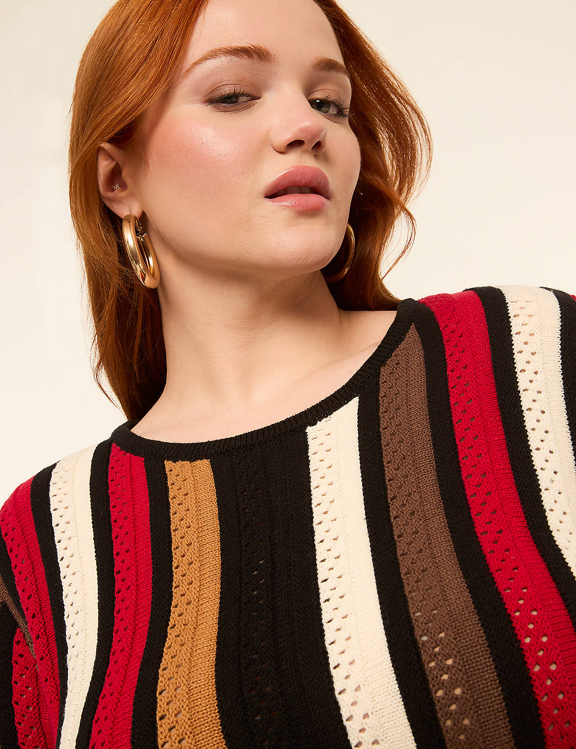 A woman with red hair and large hoop earrings wears a striped sweater against a plain, light-colored background. Product Image 4
