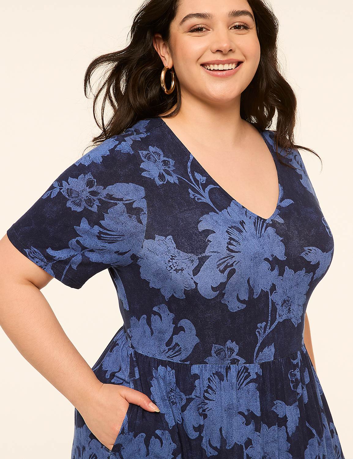 A smiling woman in a blue floral dress with her hand in her pocket stands against a plain background. Product Image 3