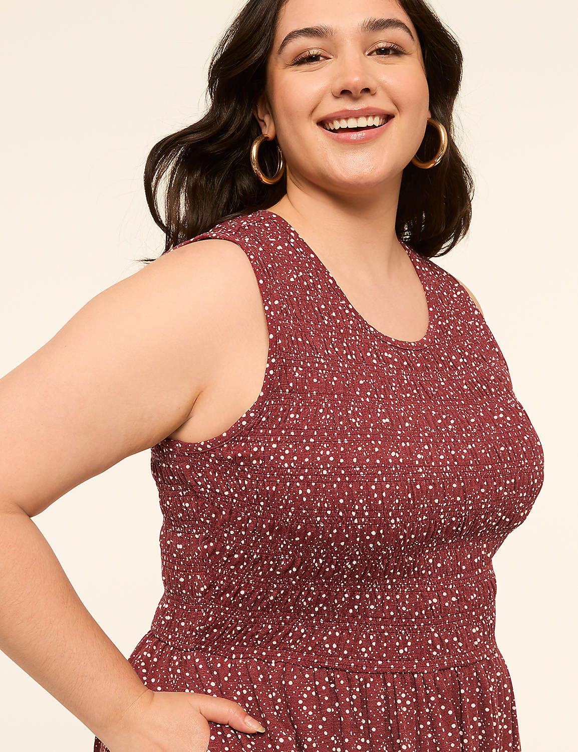 A smiling woman in a maroon polka-dot dress stands against a plain beige background. Product Image 3