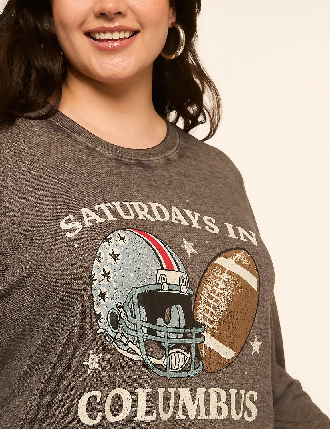 A woman smiles in the foreground, wearing a gray long-sleeved shirt with a graphic of a football helmet and ball, while the background is a plain, light-colored studio backdrop. Product Image 4