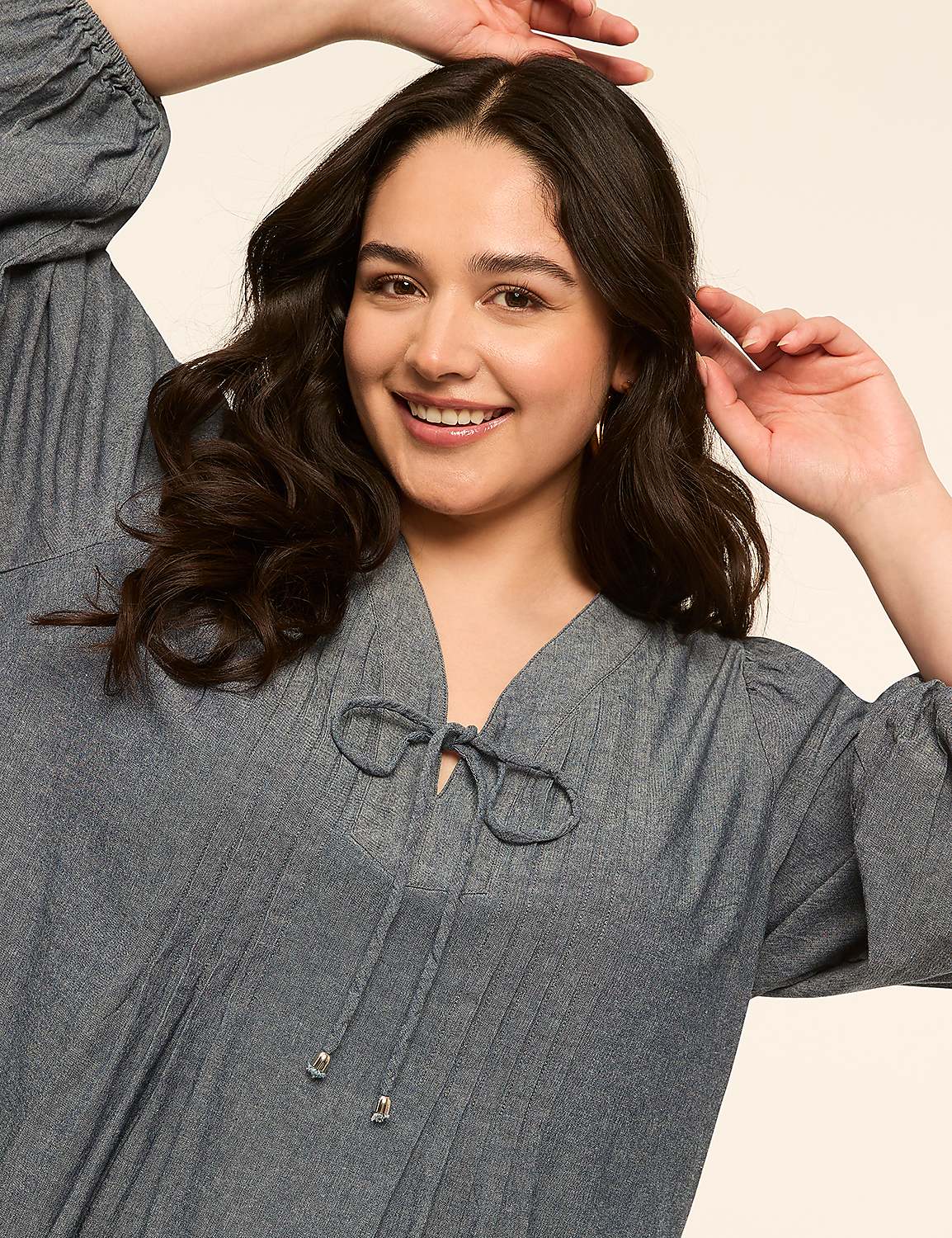 A smiling woman with dark, wavy hair and a blue dress with a tie-neck is posed against a plain, light-colored background. Product Image 3