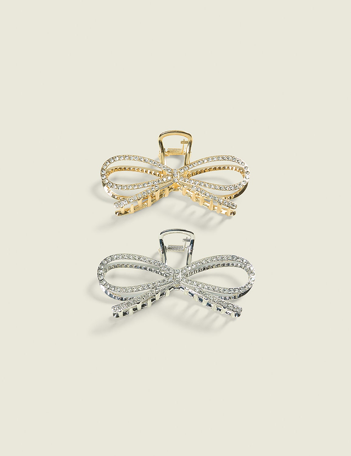 Two sparkling bow-shaped hair clips, one gold and one silver, rest on a plain, light-colored background. Product Image 1