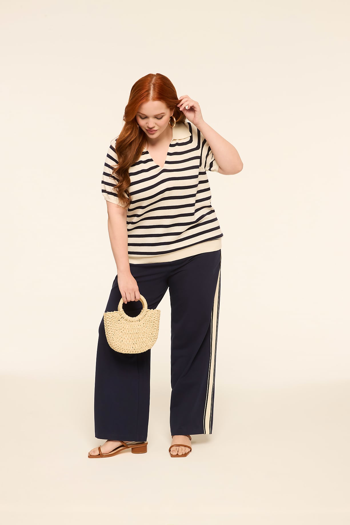 A woman with red hair stands in the foreground holding a straw bag, while the background is a plain, light-colored studio backdrop. Product Image 1