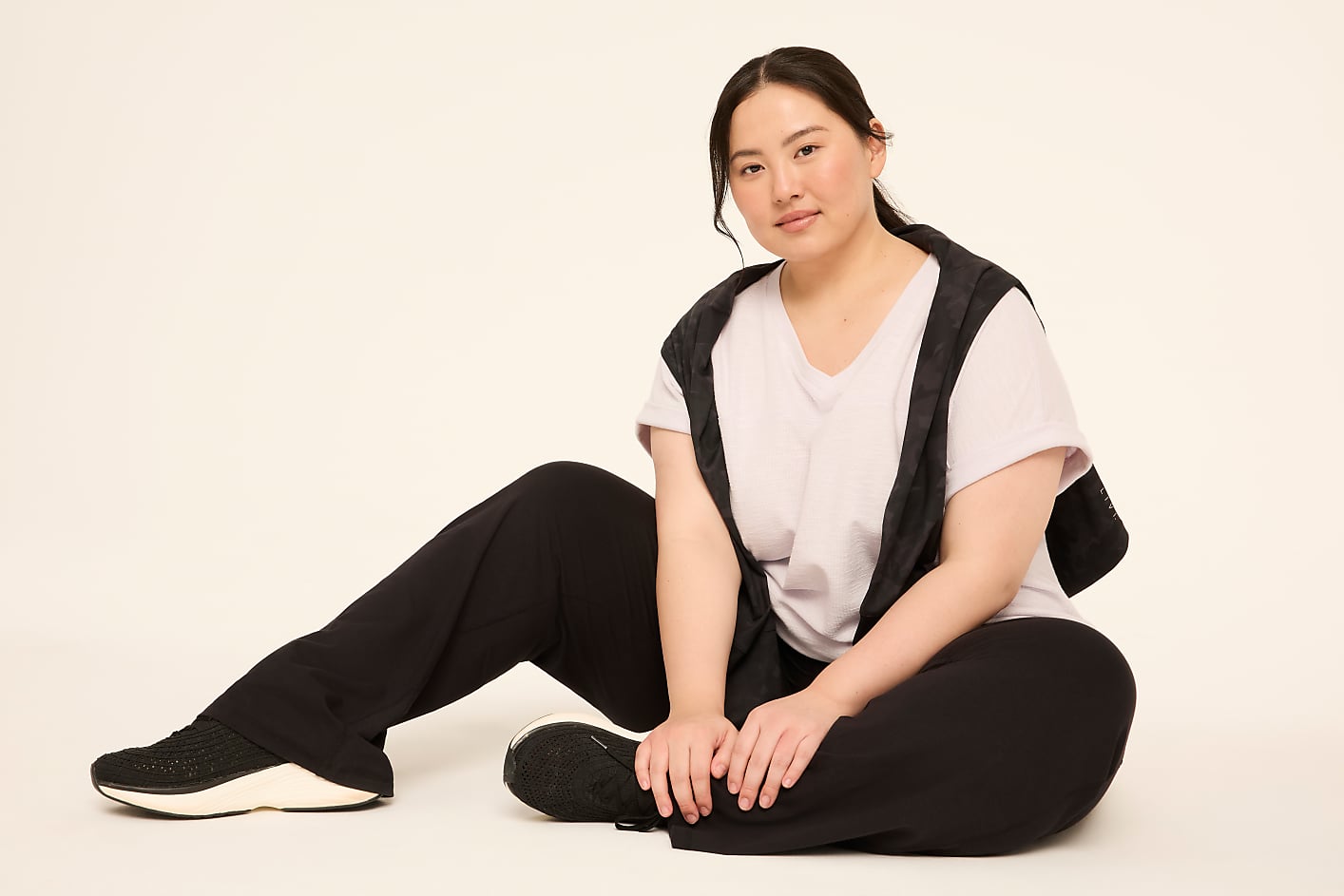 A woman in athletic wear sits on a plain, light-colored floor, with a solid, light background behind her. Product Image 7