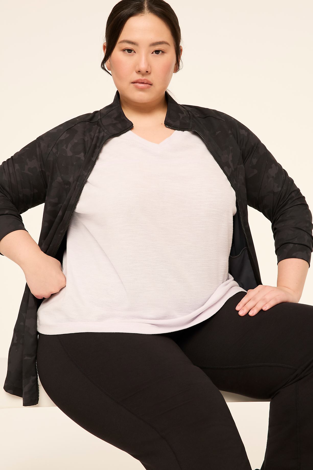 A woman in a black jacket and light purple v-neck shirt poses against a plain, light-colored background. Product Image 8
