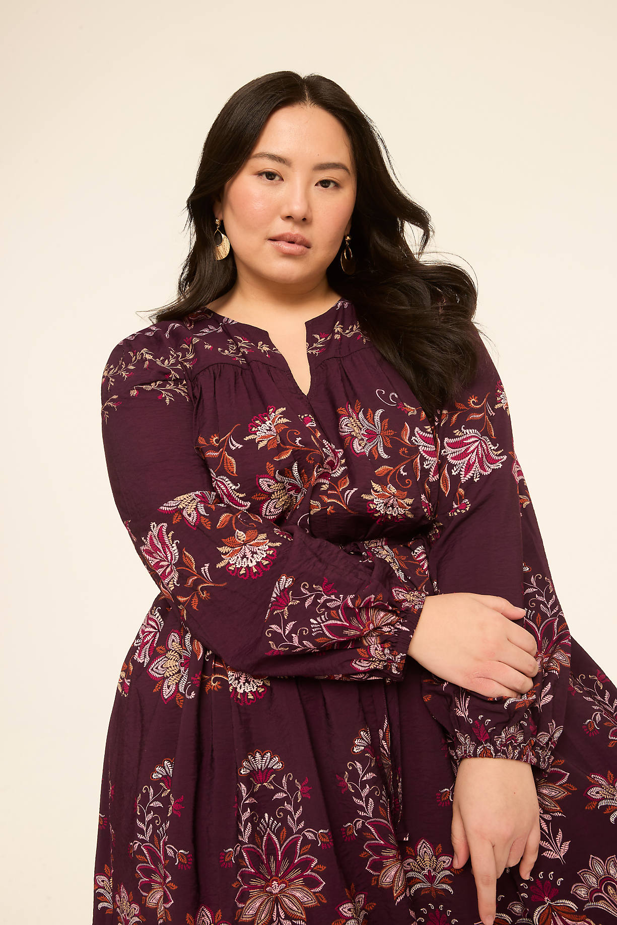 A woman in a floral print dress stands against a plain, light-colored background. Product Image 6