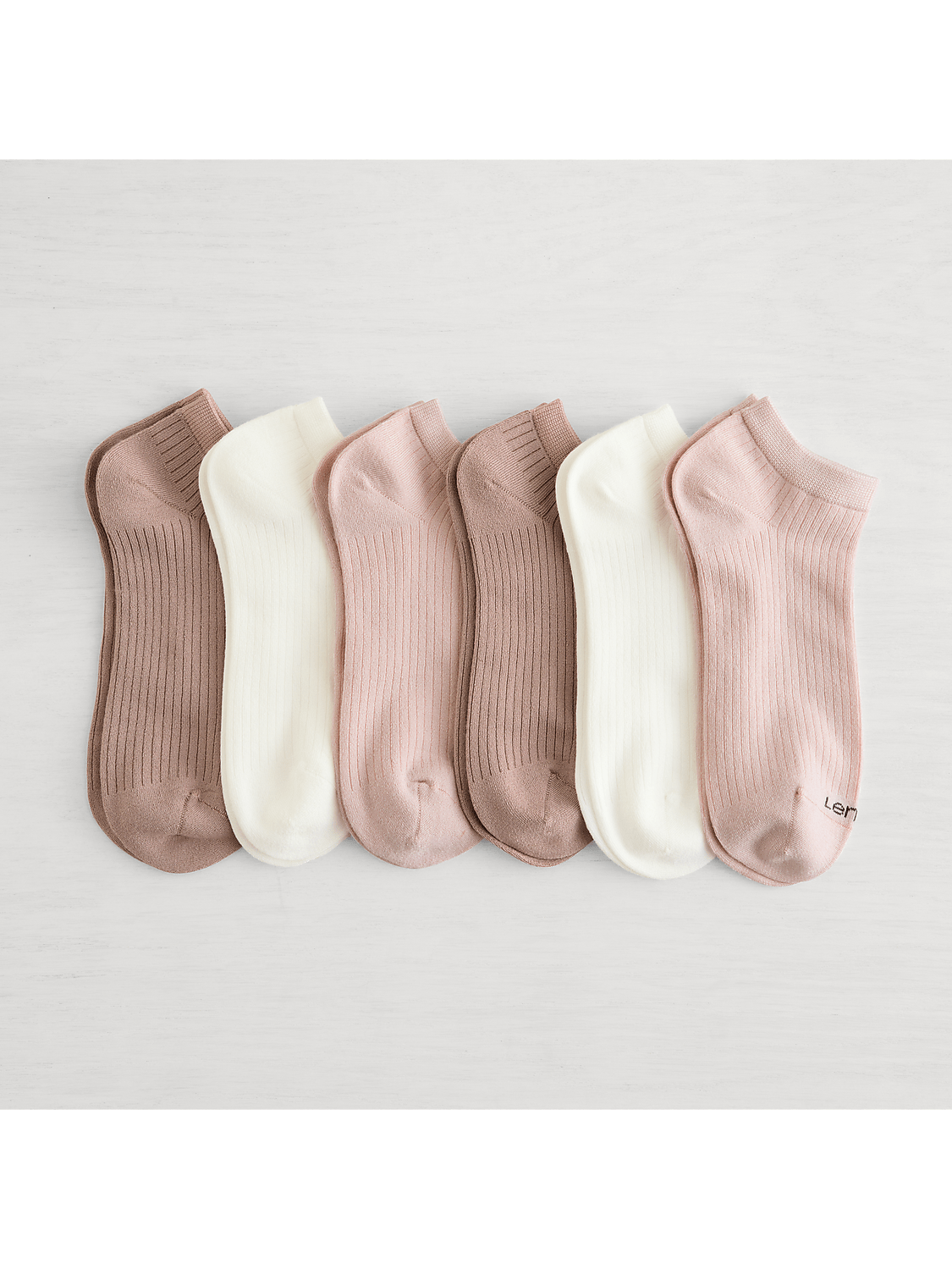 Six pairs of ribbed ankle socks in muted pink and cream hues are neatly arranged on a light, textured surface. Product Image 1