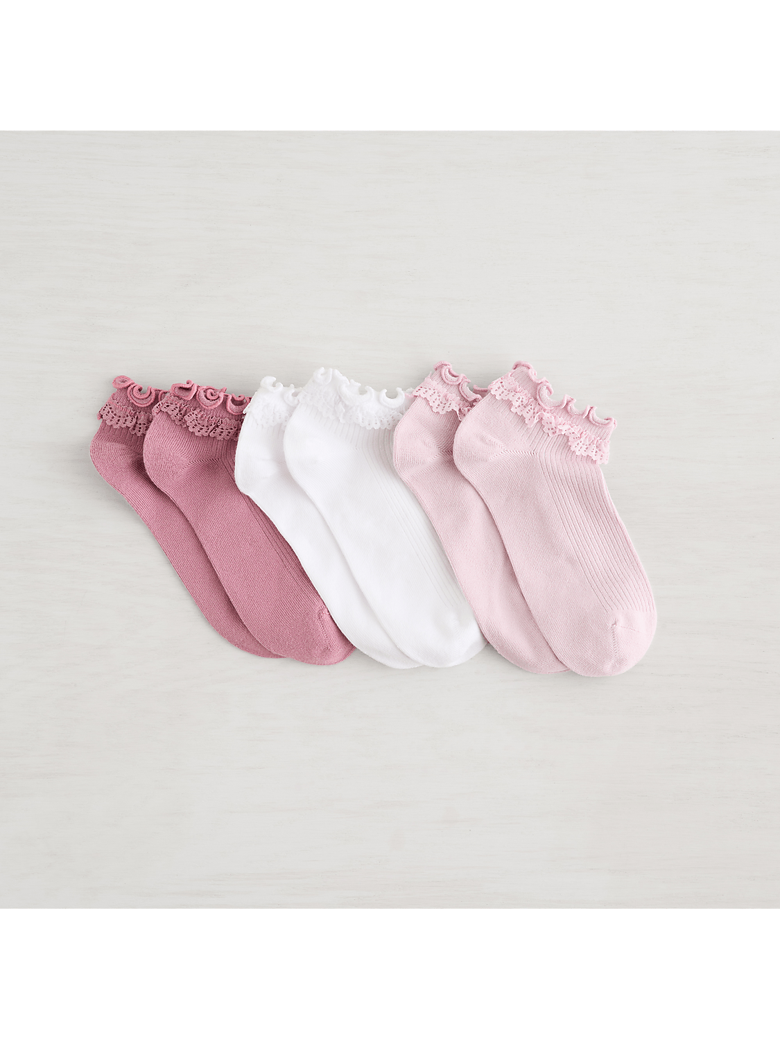 A collection of pink and white ankle socks with lace trim are arranged on a light-colored, textured surface. Product Image 3