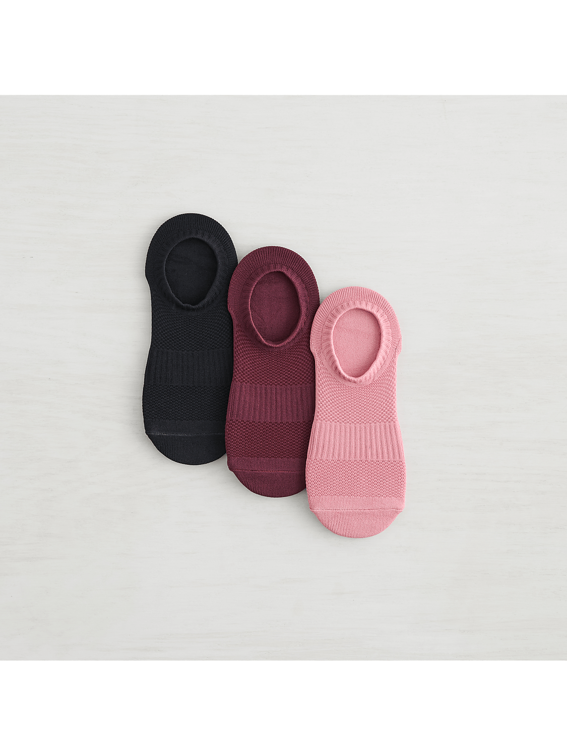 Three no-show socks in black, burgundy, and pink are arranged on a light gray, textured surface. Product Image 5