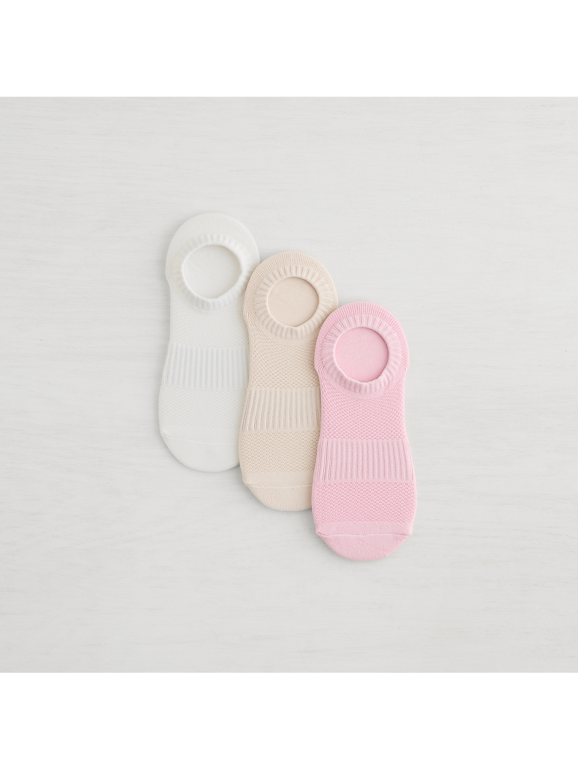 Three no-show socks in white, beige, and pink are arranged on a white wooden surface. Product Image 3