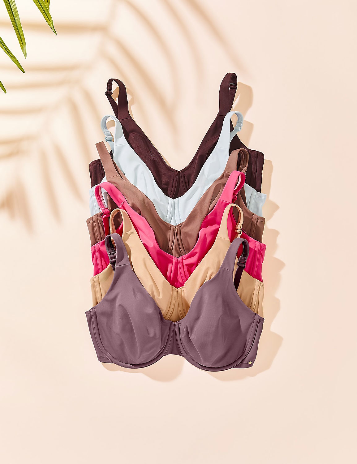 A stack of colorful bras lies on a light peach background, with palm frond shadows cast from the upper left. Product Image 5