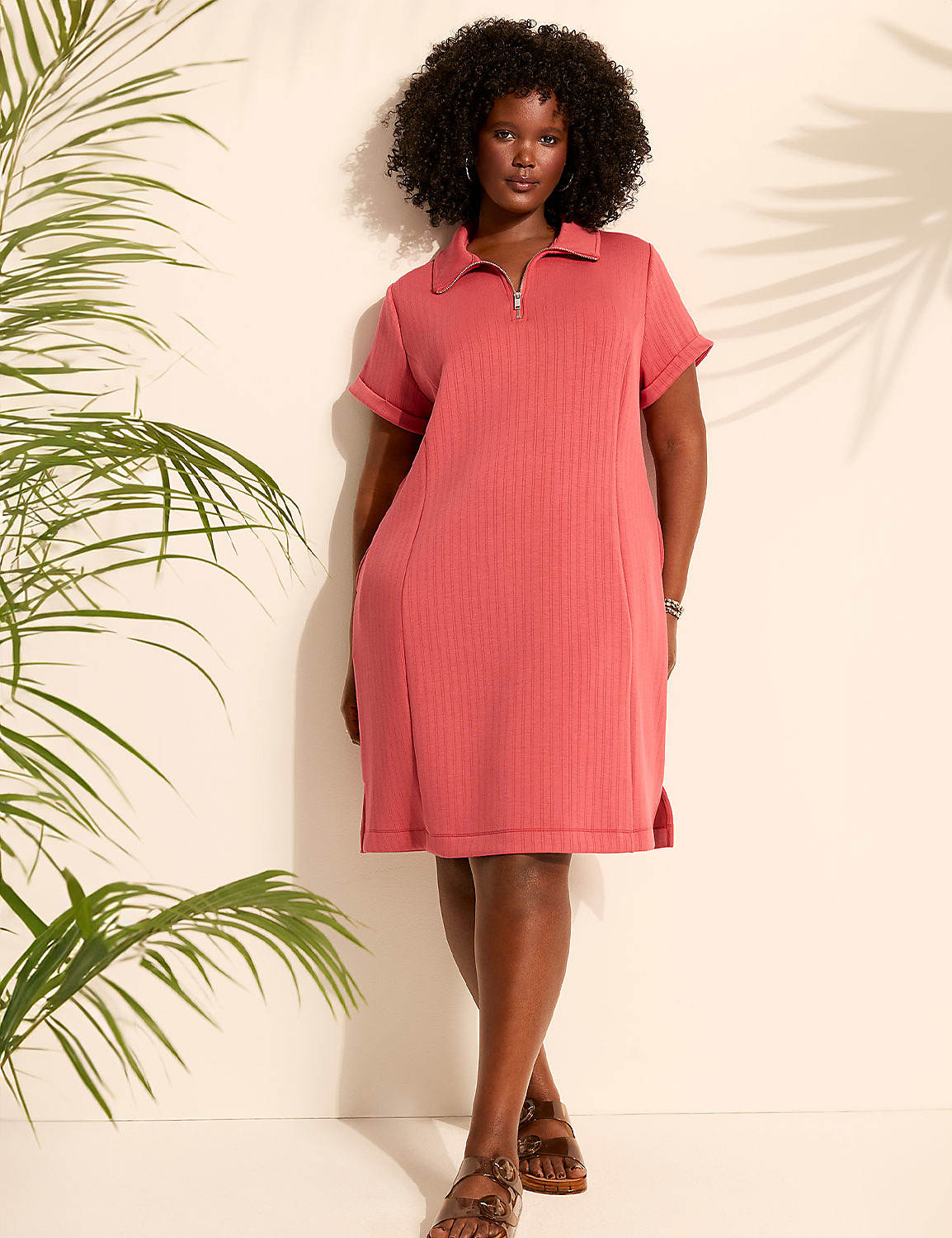 A woman in a coral polo dress stands against a light wall with palm fronds casting shadows in the background. Product Image 4