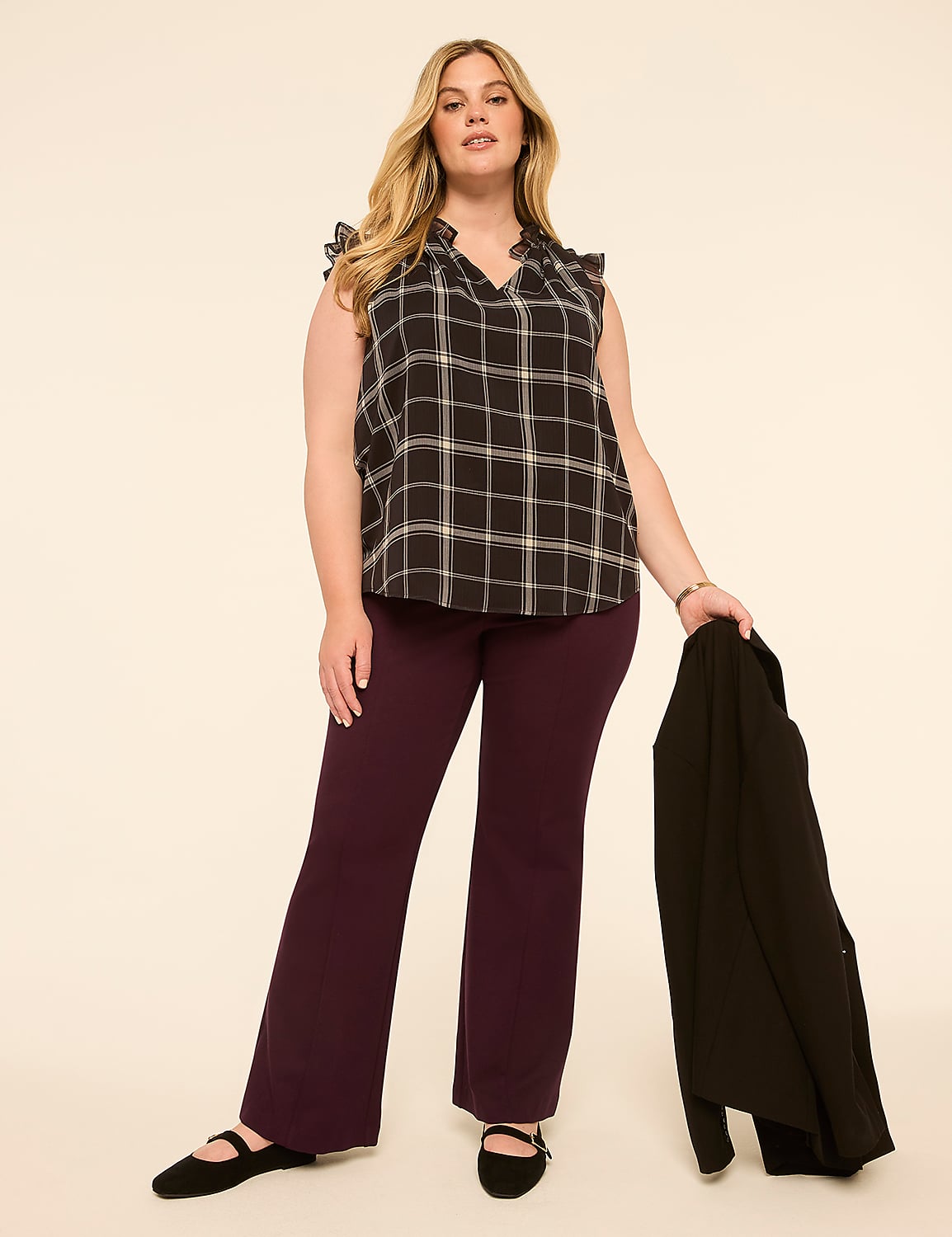A woman in a plaid top and plum pants stands against a plain, light-colored background, holding a black blazer. Product Image 3