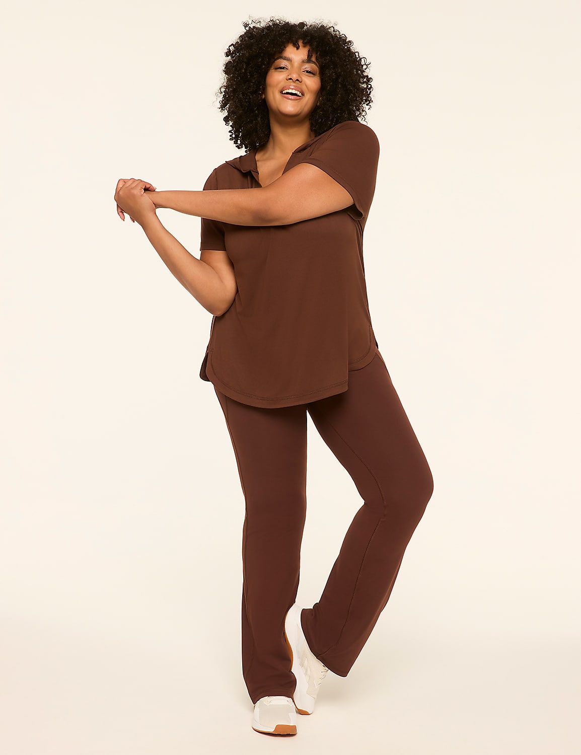 A smiling woman in a brown loungewear set stretches her arms in front of a plain, light-colored background. Product Image 3