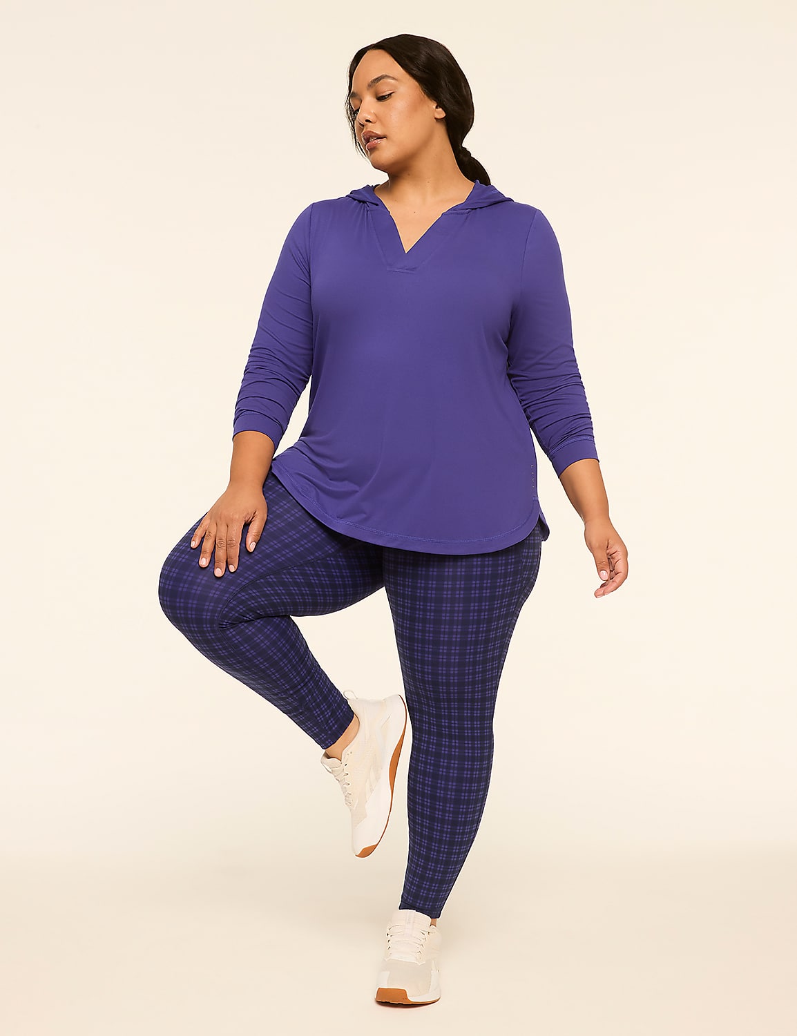 A woman in a purple hooded top and plaid leggings stands on one leg against a plain, light-colored background. Product Image 3