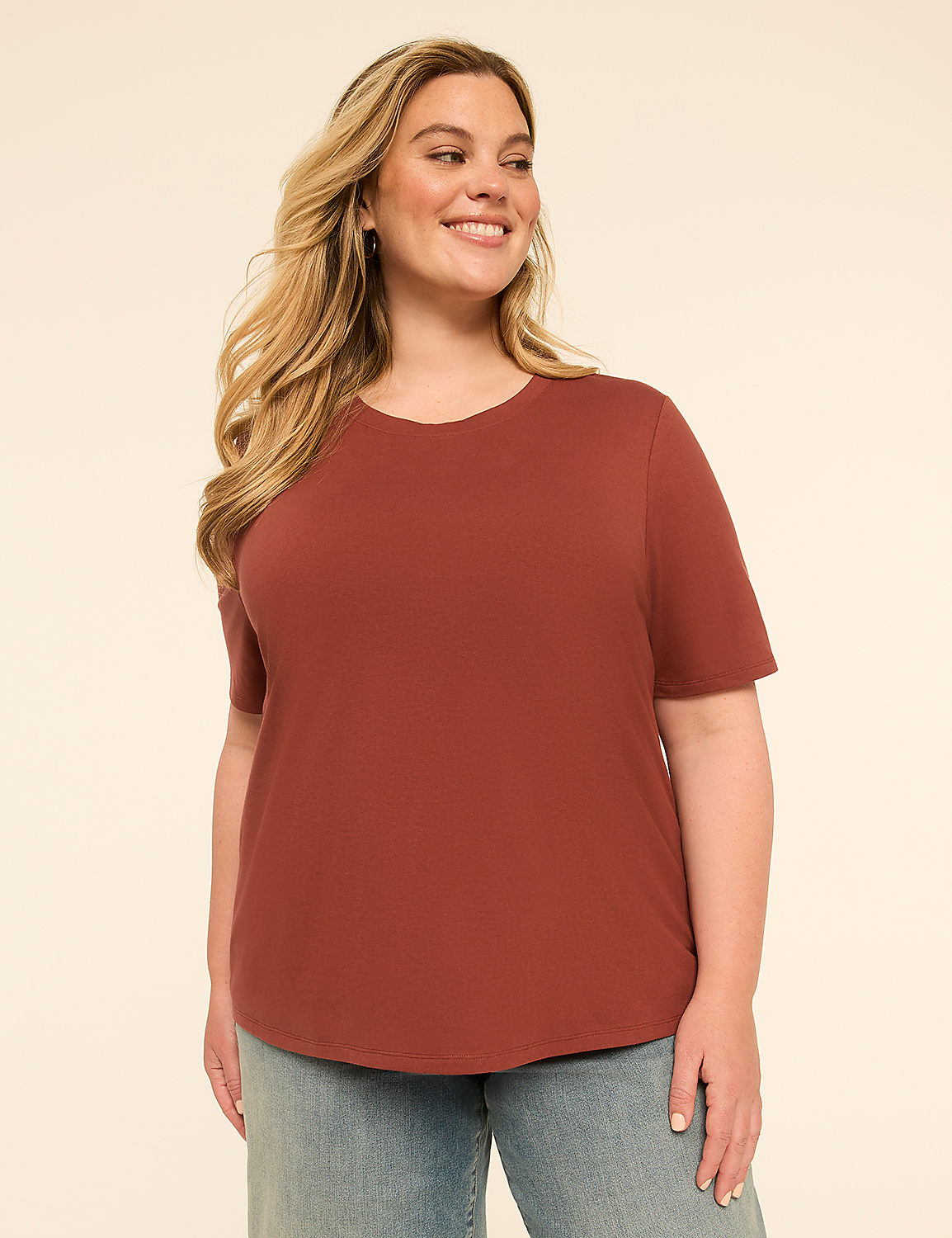 A smiling woman in a rust-colored t-shirt and denim shorts stands against a plain, light-colored background. Product Image 1