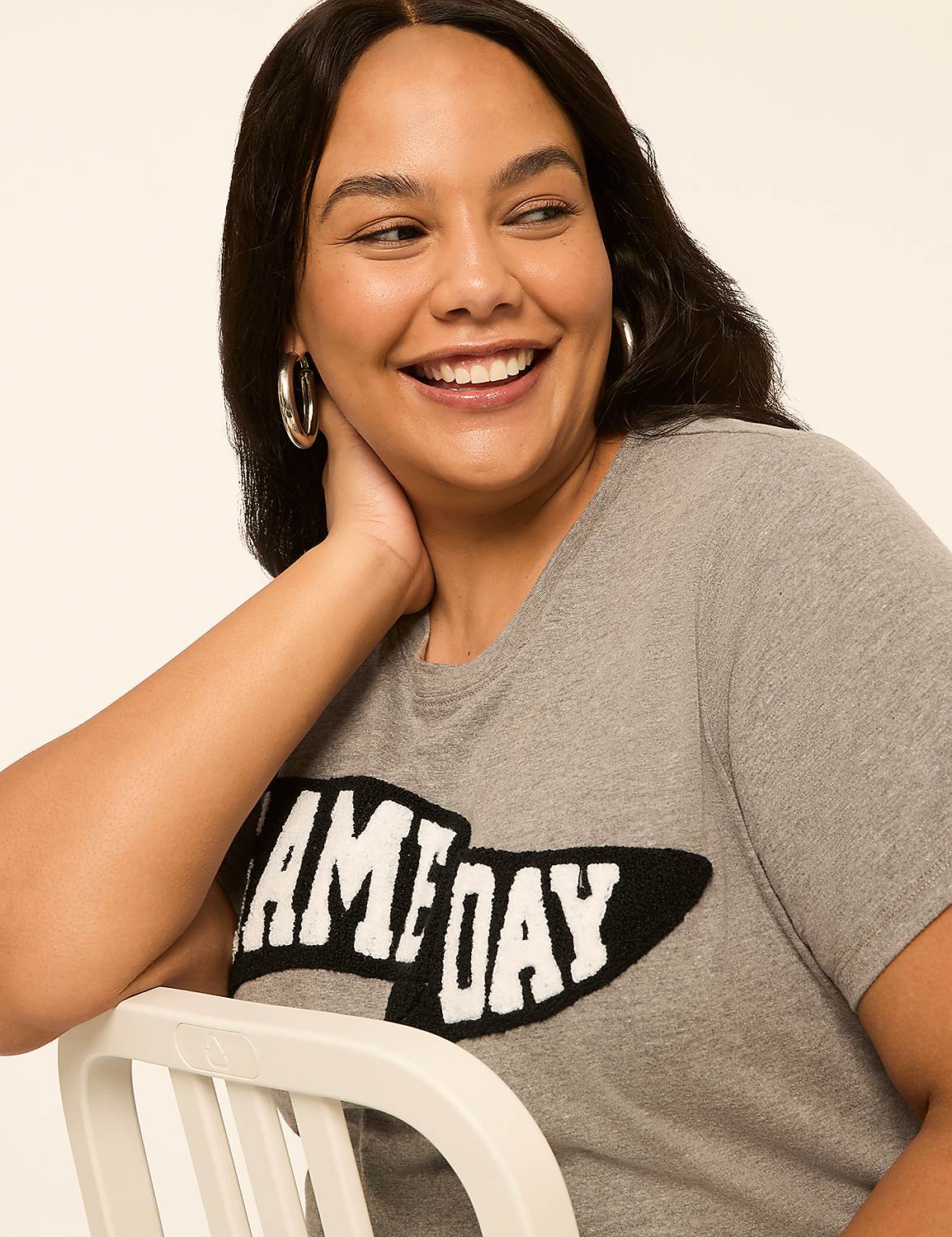 A woman with hoop earrings smiles as she wears a grey t-shirt with "GAME DAY" emblazoned across the front against a plain background. Product Image 4