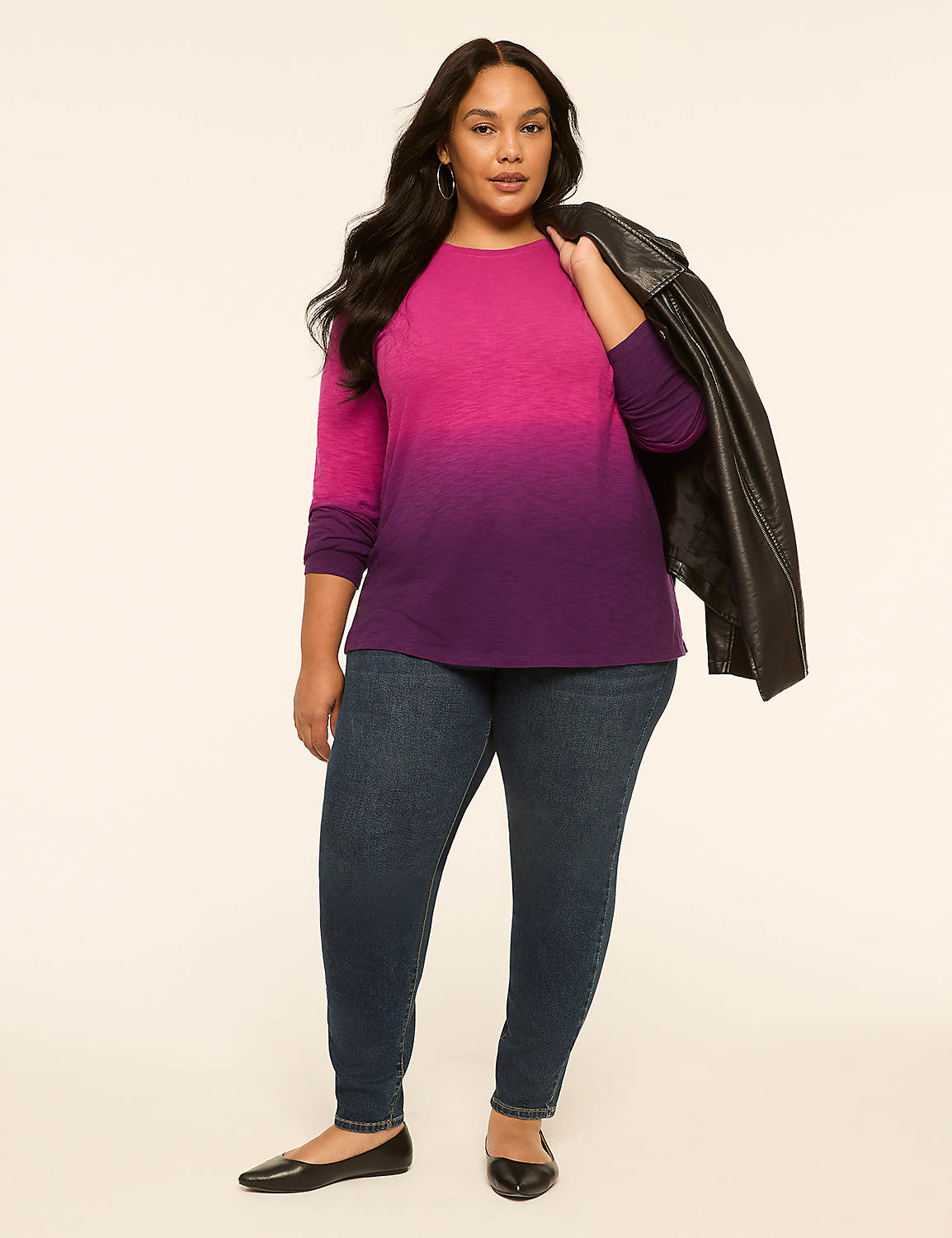 A woman in a pink and purple ombre shirt and jeans stands against a plain, light-colored background with a black leather jacket draped over her shoulder. Product Image 3