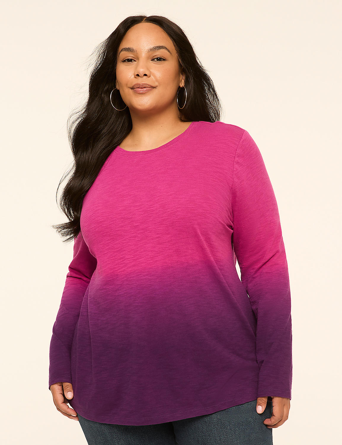 A woman with long dark hair and hoop earrings poses in a long-sleeved, ombre pink and purple shirt against a plain, light-colored background. Product Image 1