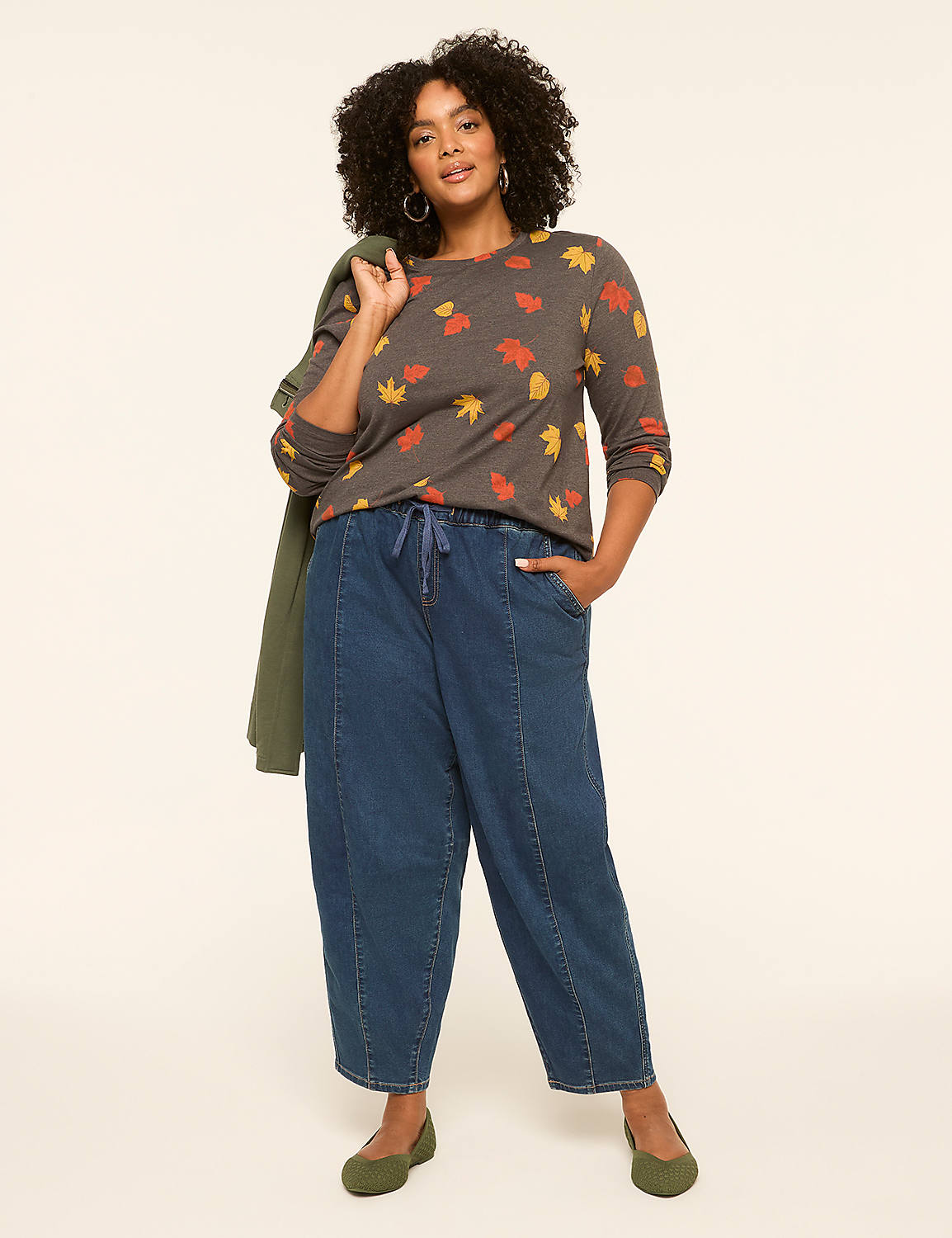 A woman with curly dark hair stands in the foreground wearing a leaf-patterned shirt and wide-leg jeans, with a plain, light-colored background behind her. Product Image 3