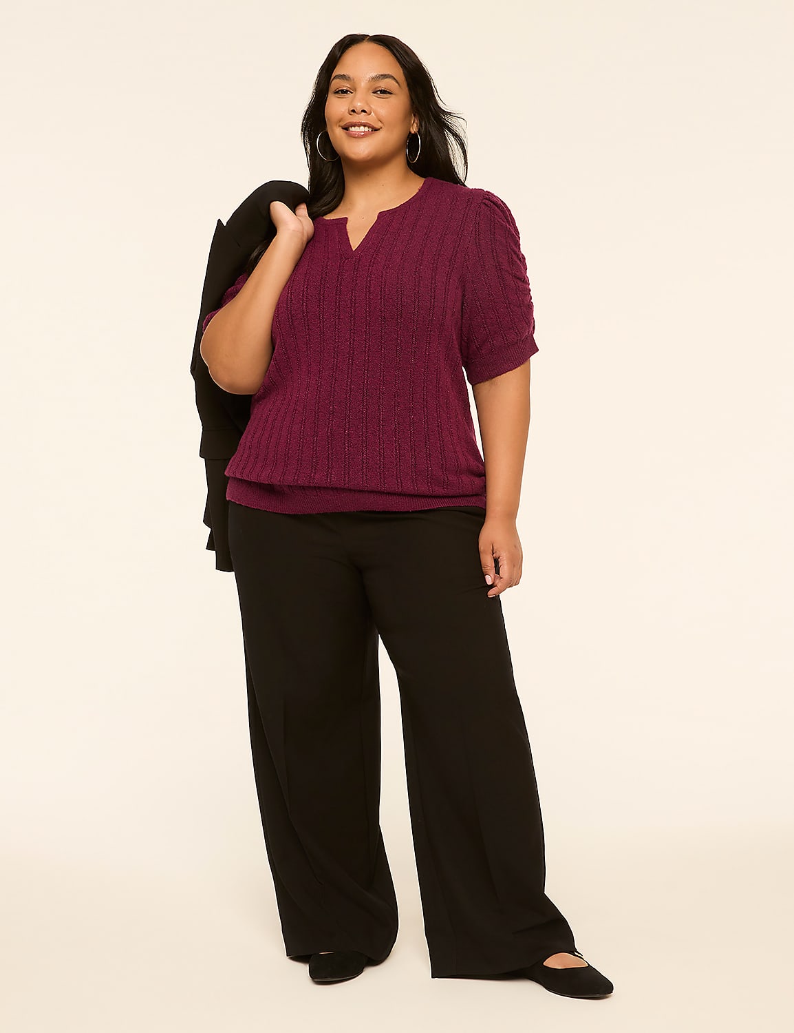 A woman in a purple top and black pants stands against a plain, light-colored background, with a black jacket draped over her shoulder. Product Image 3