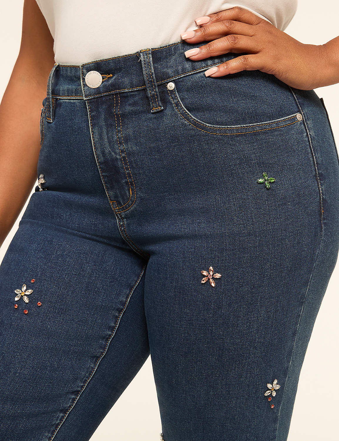 A close-up of dark wash denim jeans adorned with colorful floral embellishments in the foreground, with a plain, light-colored background. Product Image 4