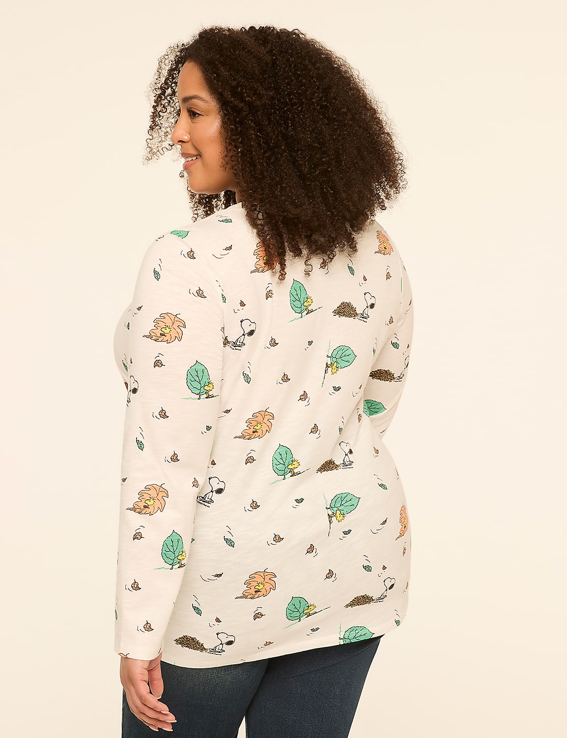 A woman with curly hair, wearing a long-sleeved shirt with a pattern of Snoopy and Woodstock, stands against a plain, light-colored background. Product Image 2