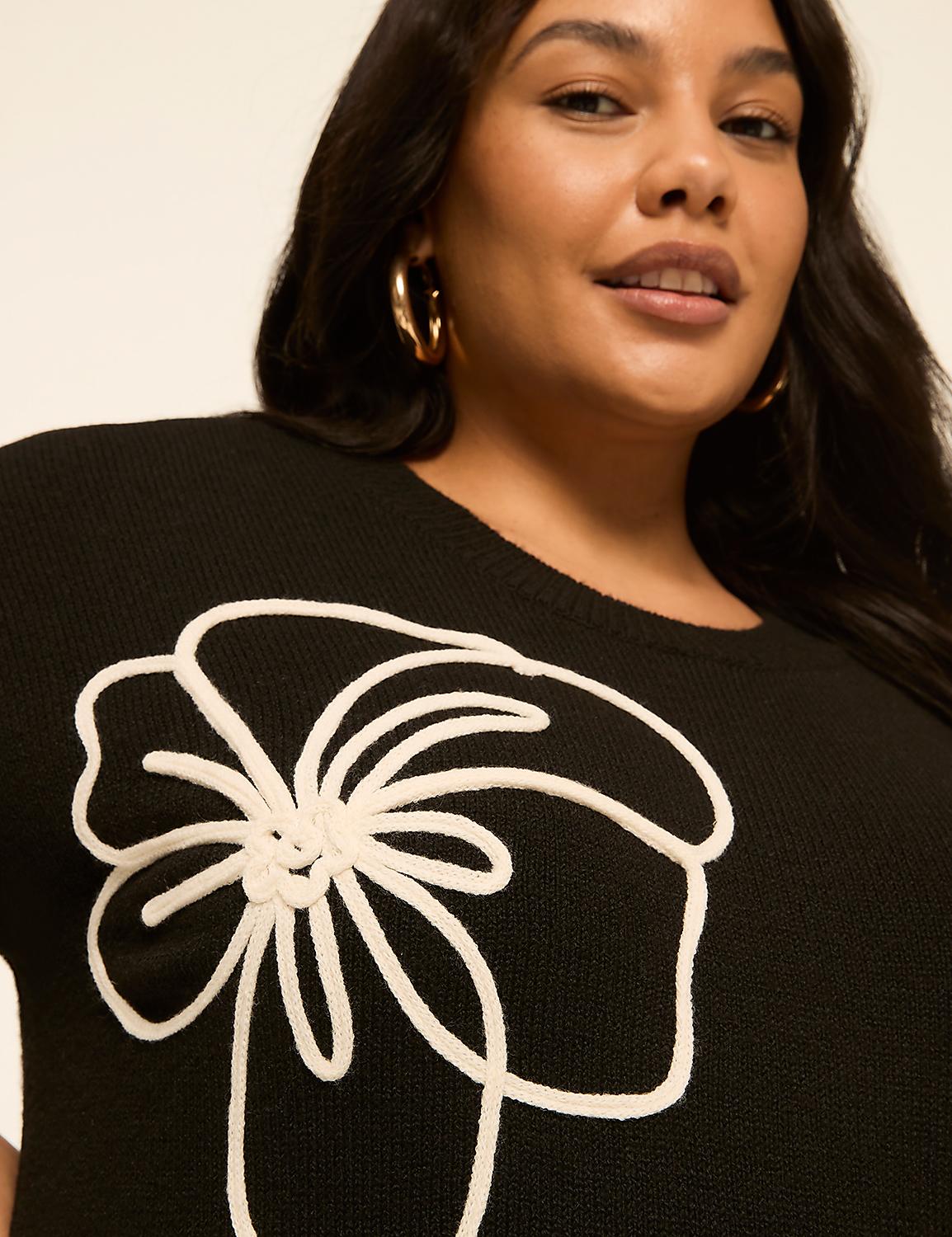 A woman with dark hair and hoop earrings smiles as she wears a black sweater with a white floral design, set against a plain background. Product Image 4