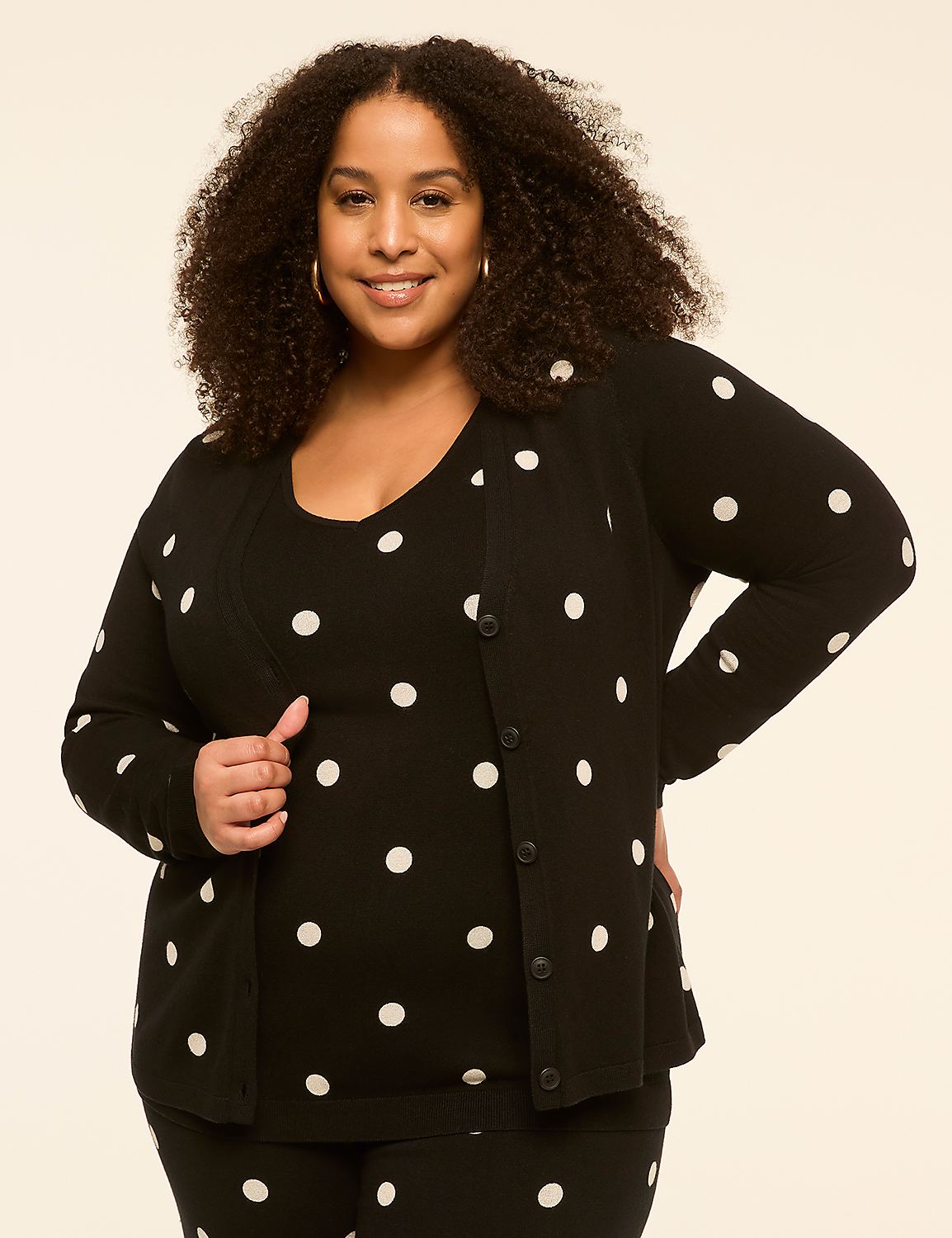 A smiling woman with curly hair poses in a black and white polka dot outfit against a plain, light-colored background. Product Image 1