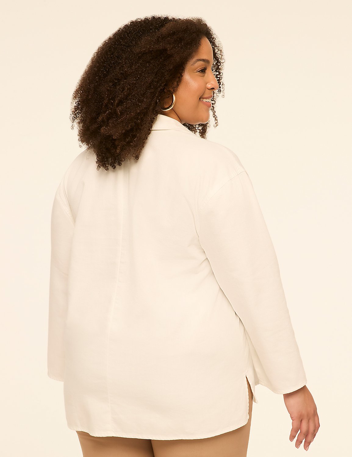 A woman with curly brown hair, wearing a white collared shirt and tan pants, smiles over her shoulder against a plain cream background. Product Image 2