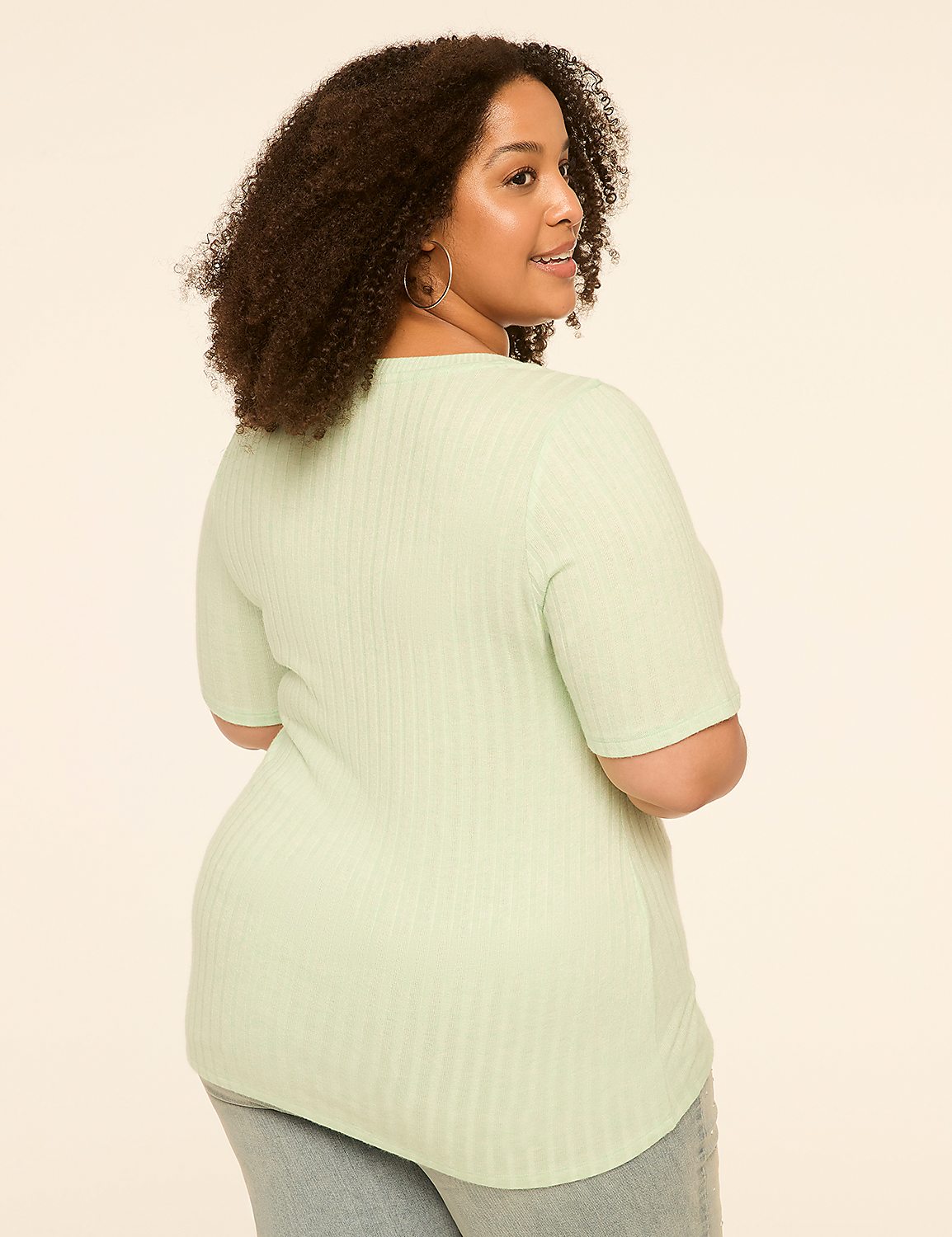 A woman with curly hair in a light green ribbed shirt stands against a plain, light-colored background. Product Image 2