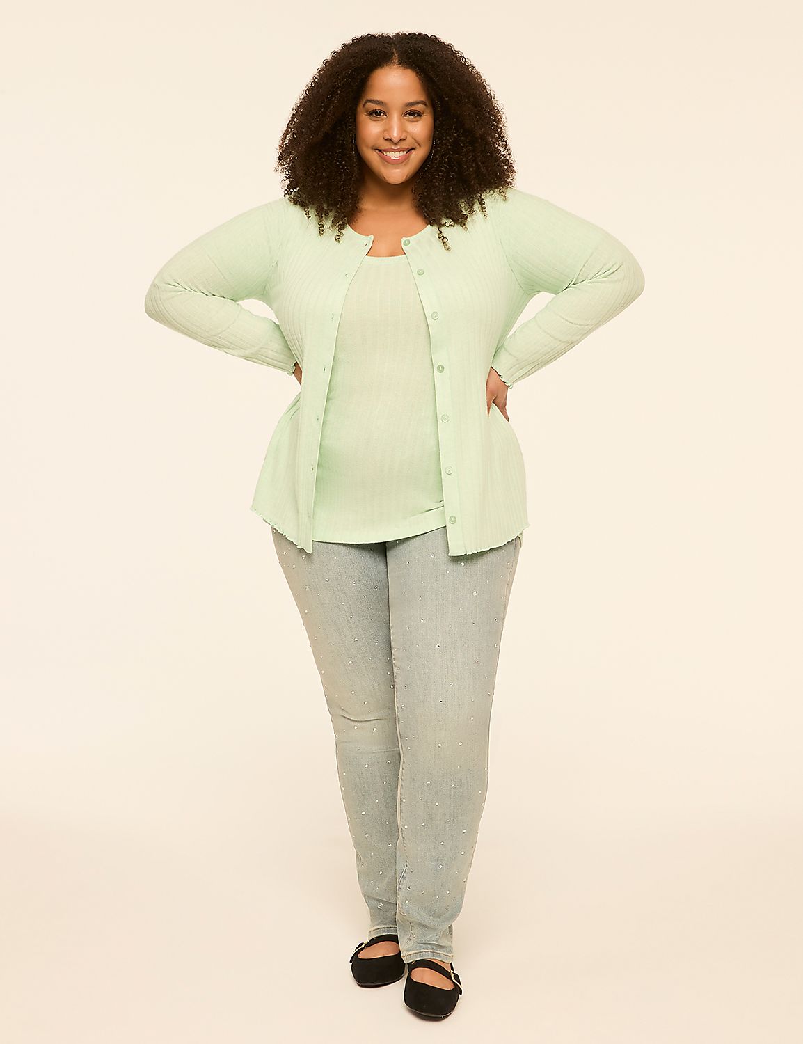 A smiling woman with curly hair stands in the foreground wearing a light green cardigan and jeans against a plain, light-colored background. Product Image 3