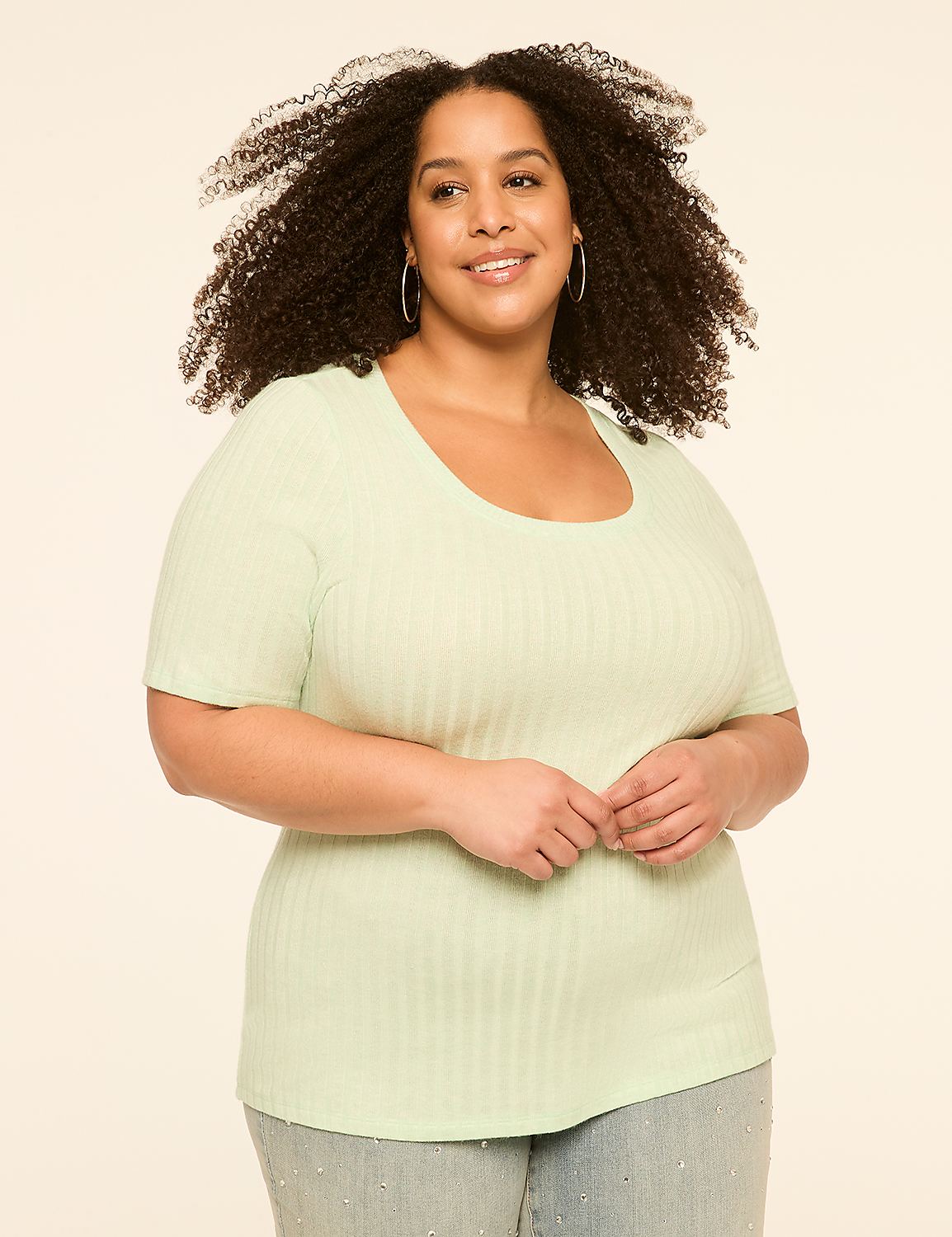 A smiling woman with curly hair in a light green ribbed shirt stands against a plain, light-colored background. Product Image 1
