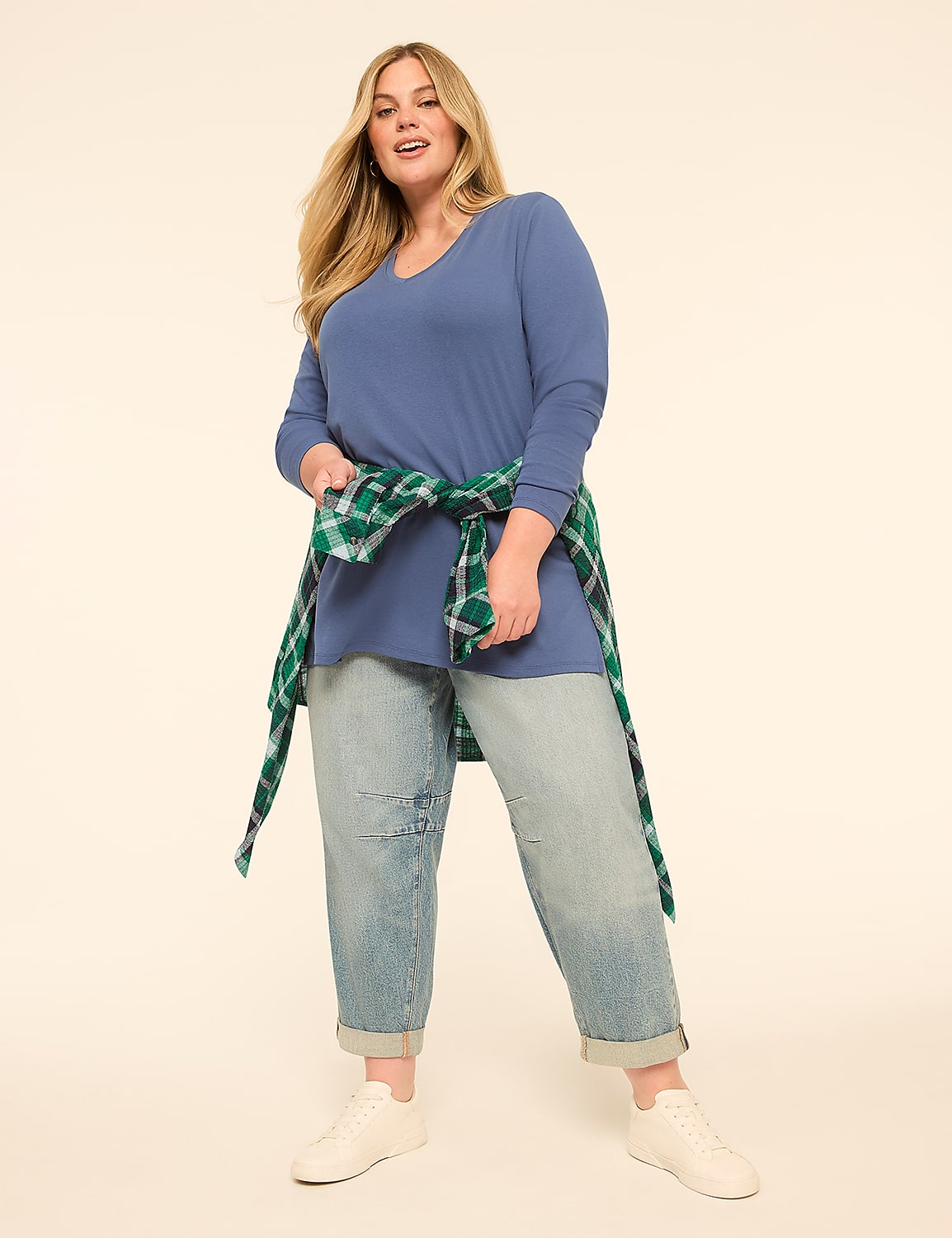 A woman in a blue tunic and jeans stands against a plain, light-colored background, with a green and white plaid shirt tied around her waist. Product Image 3