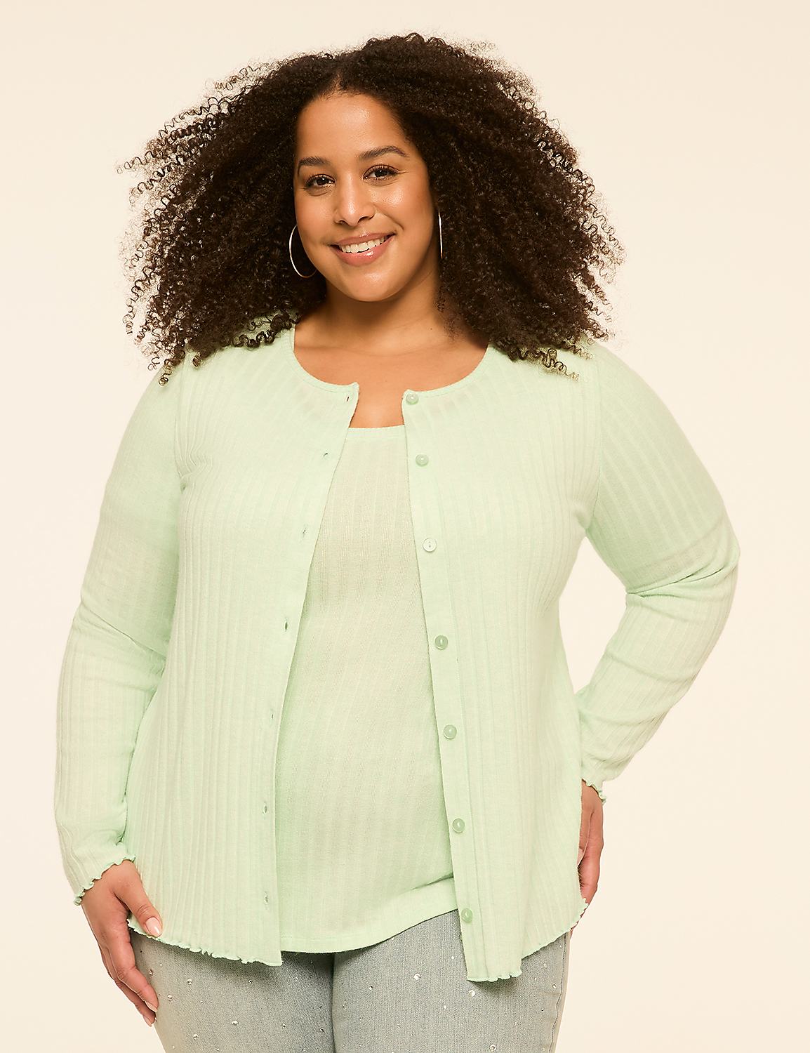 A smiling woman with curly hair wears a light green cardigan and tank top in the foreground, against a plain, light-colored background. Product Image 1