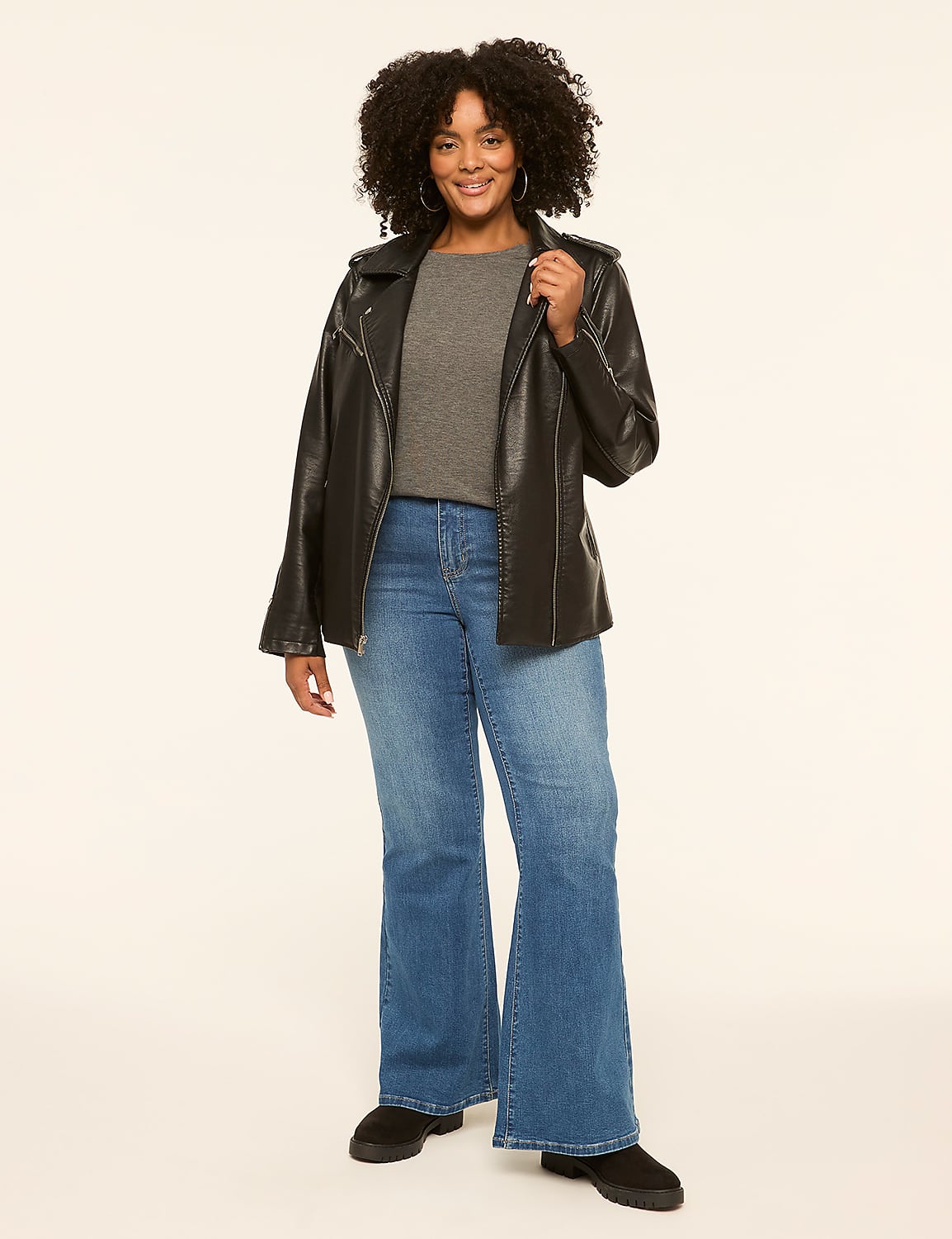 A smiling woman in a black leather jacket and blue flared jeans stands against a plain, light-colored background. Product Image 3