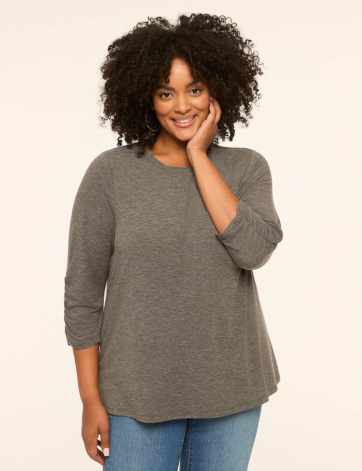 A smiling woman with curly dark hair and a grey shirt poses against a plain cream background. Product Image 1
