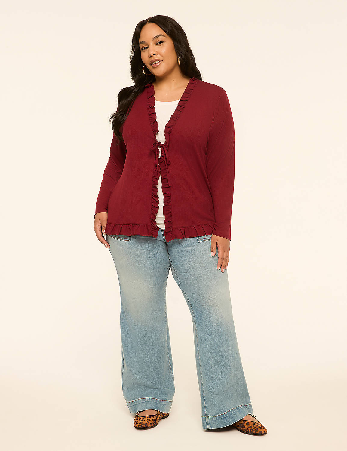 A woman in a maroon ruffled cardigan and light wash flared jeans stands against a plain cream background. Product Image 3