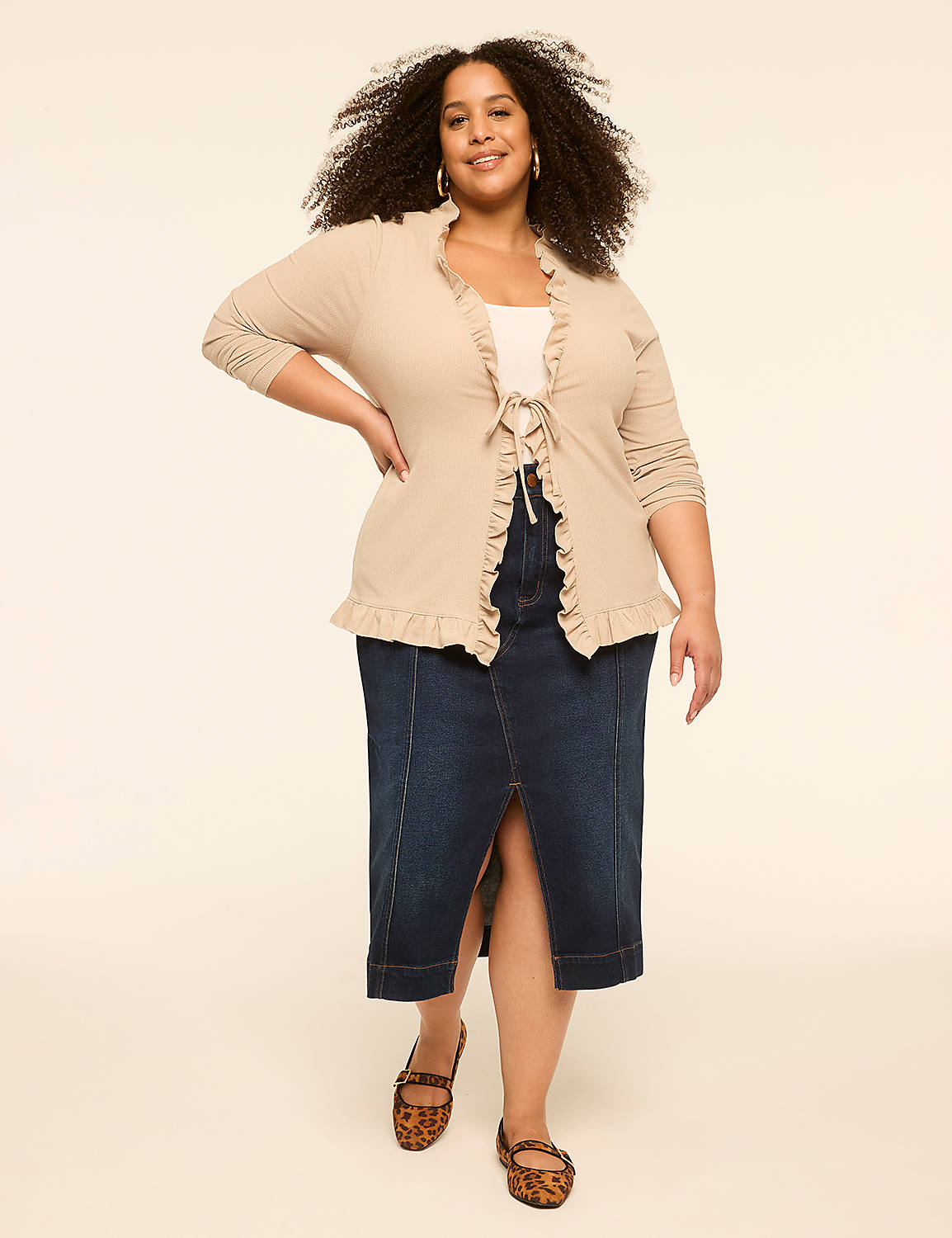 A smiling woman in a beige ruffled cardigan and denim skirt stands against a plain cream background. Product Image 3