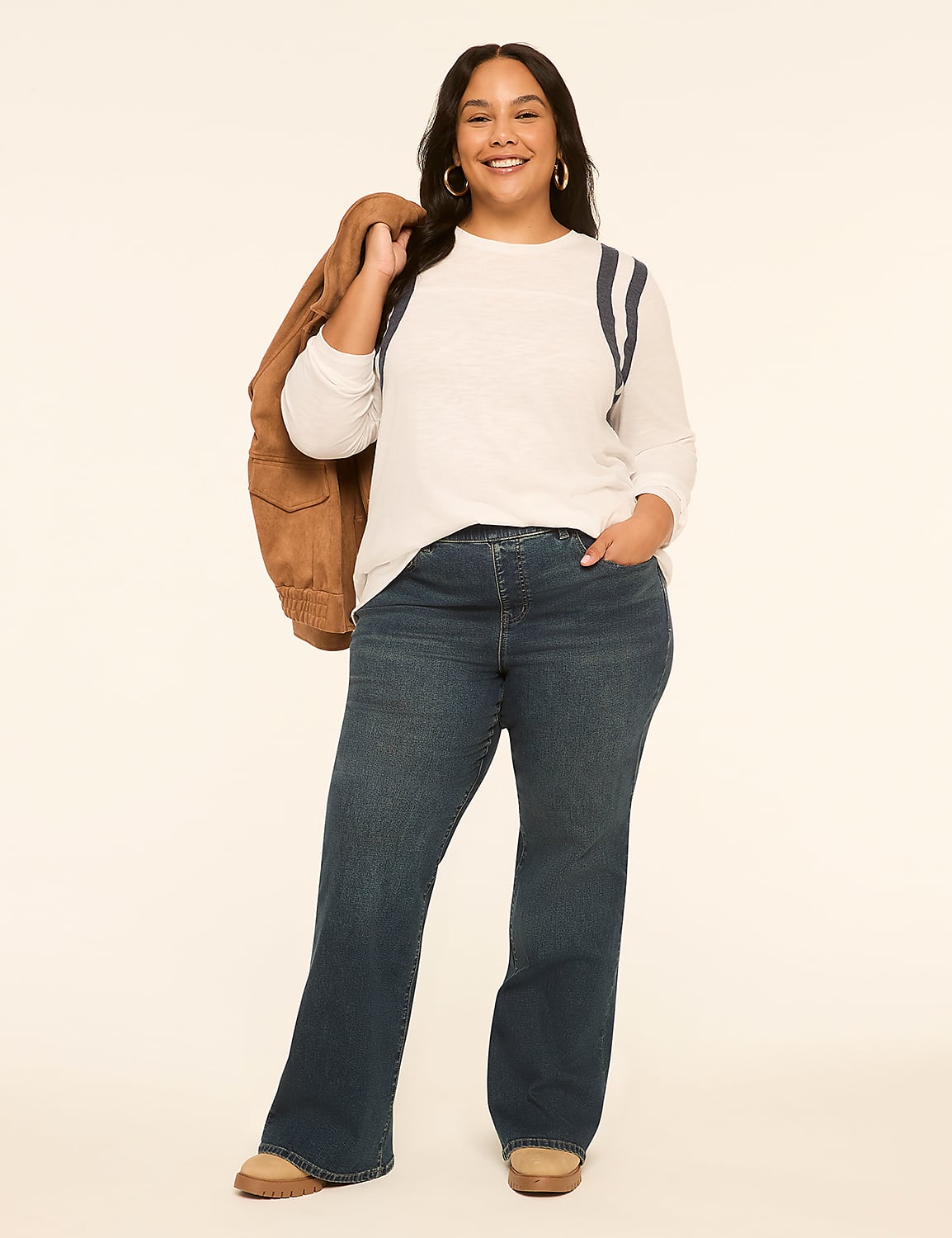 A smiling woman in a white top and blue jeans stands against a plain, light-colored background, with a brown jacket slung over her shoulder. Product Image 3