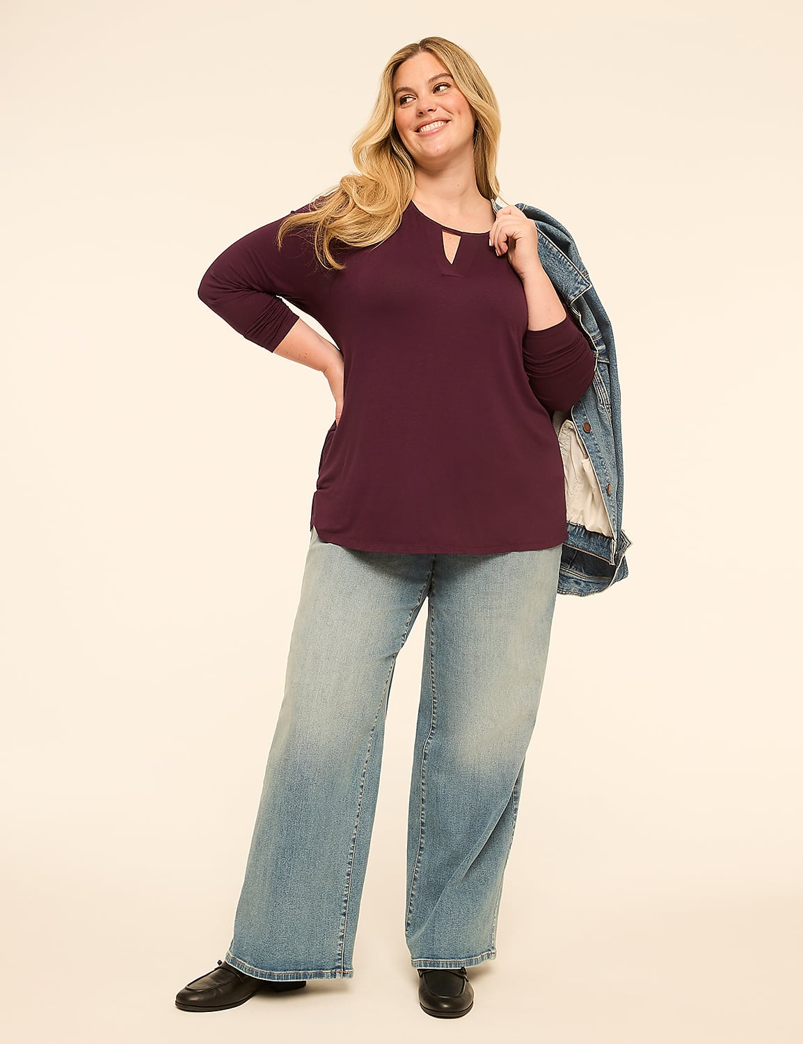 A smiling woman in a plum top and wide-leg jeans stands against a plain, light-colored background with a denim jacket draped over her shoulder. Product Image 3