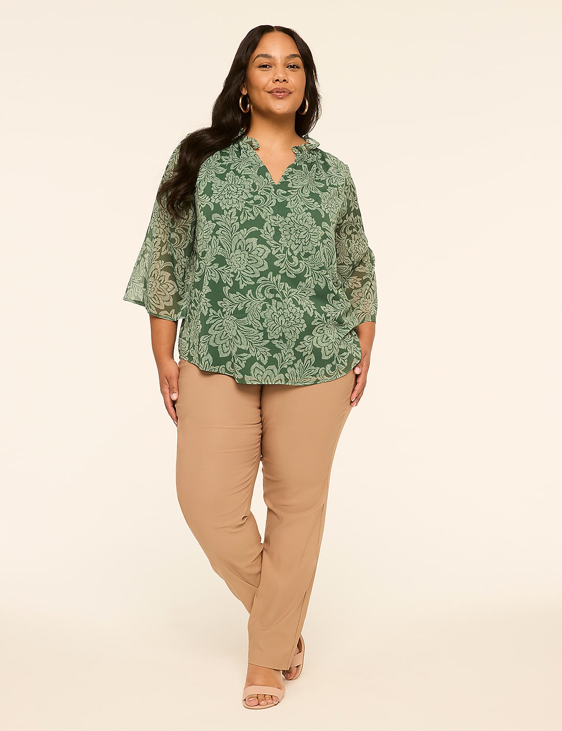 A woman in a green patterned blouse and tan pants stands against a plain, light background. Product Image 3