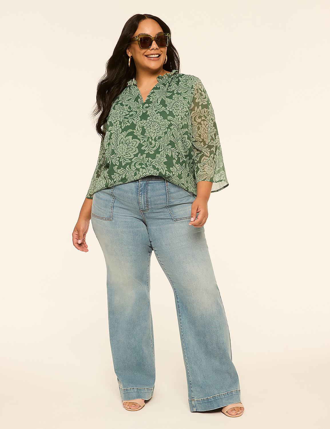 A smiling woman in a green floral blouse and light-wash wide-leg jeans stands against a plain, light-colored background. Product Image 4