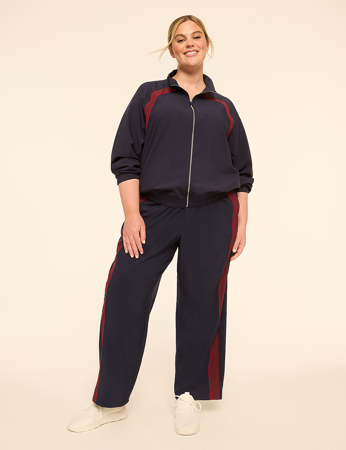 A smiling woman in a navy tracksuit with maroon stripes stands against a plain, light-colored background. Product Image 3