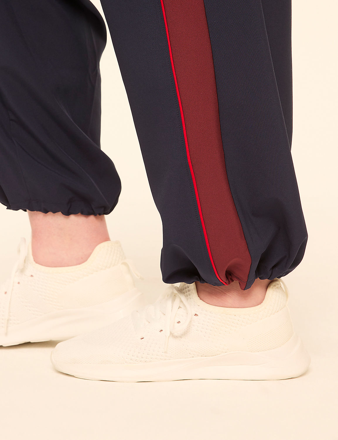 Cream sneakers are worn with navy blue pants featuring a maroon stripe, against a plain cream background. Product Image 4