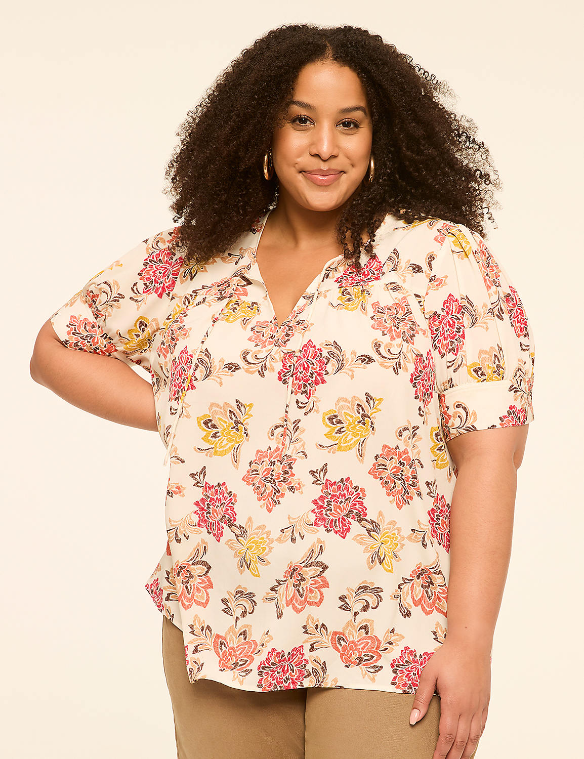A woman with curly dark hair smiles confidently in a floral blouse, standing against a plain, light-colored background. Product Image 1
