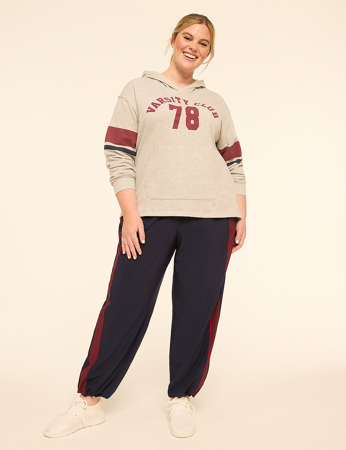 A smiling woman in a grey hoodie and navy sweatpants stands against a plain, light-colored background. Product Image 3