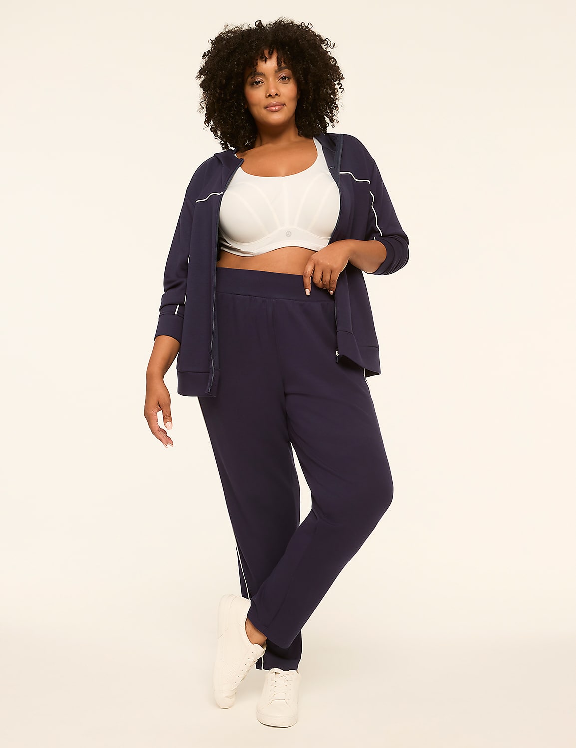 A woman in a navy tracksuit and white sports bra stands against a plain cream background. Product Image 3