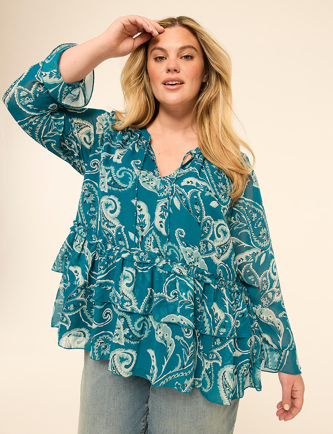 A woman in a teal paisley-print ruffled blouse and jeans poses against a plain beige background. Product Image 1